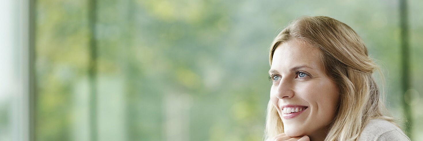 Junge Frau am Computer sitzend schaut lächelnd aus dem Fenster 