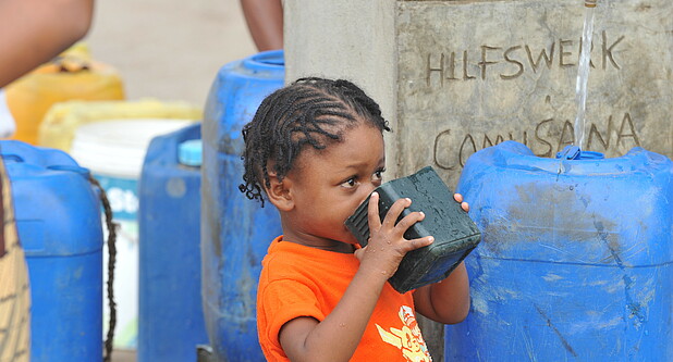 Kind in Mosambik trinkt Wasser vor Hilfswerk Brunnen